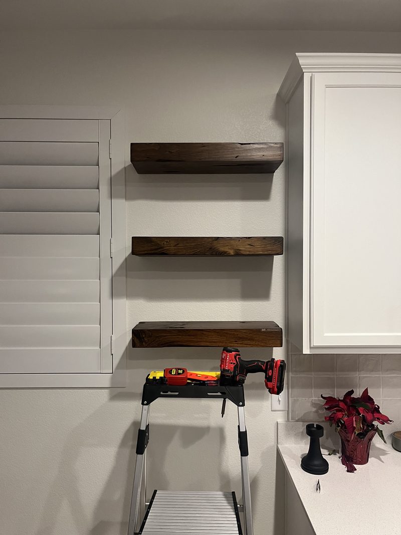 Three stained floating shelves installed level in a kitchen